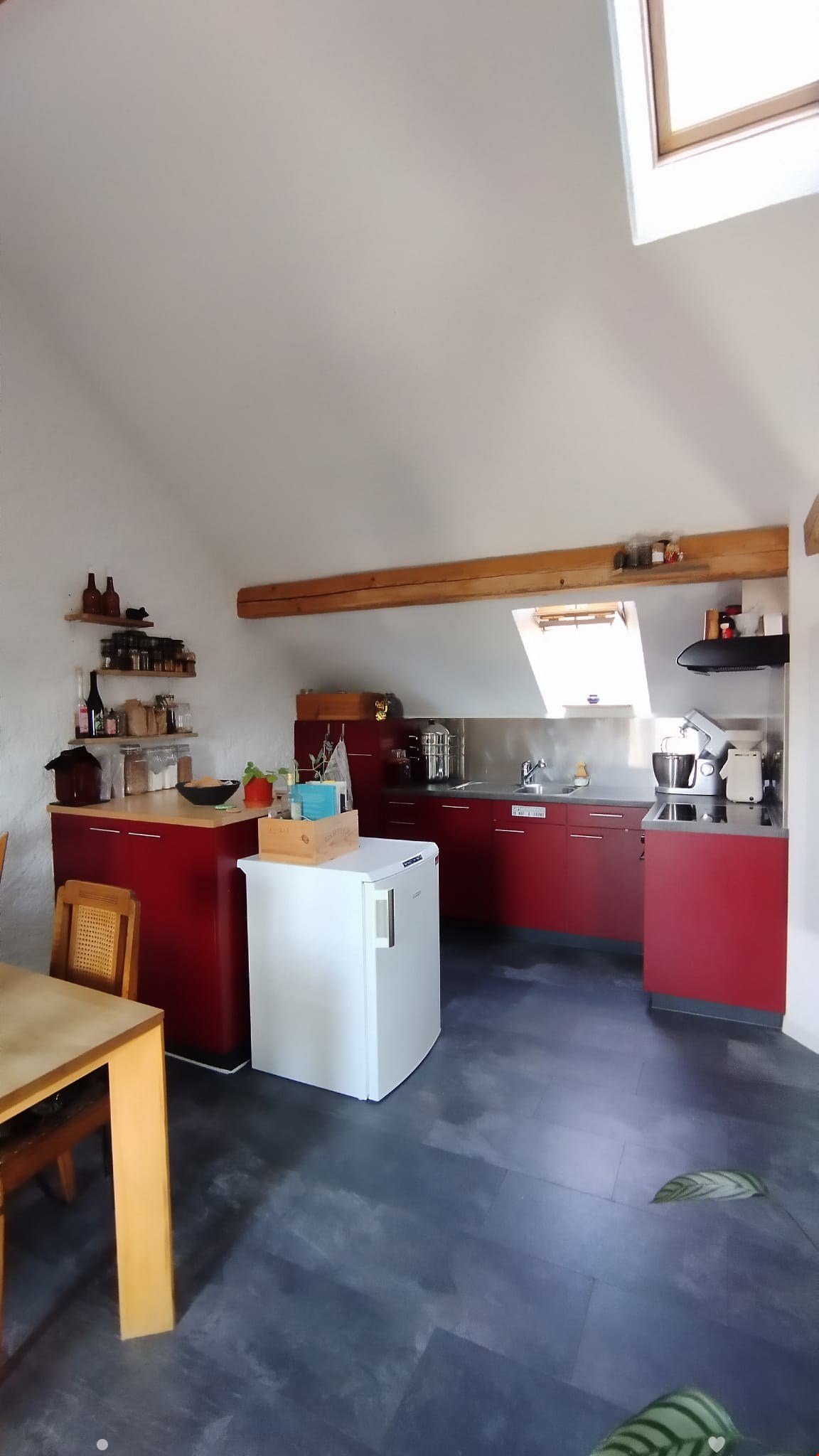 Modern kitchen with red cabinets, white refrigerator, wooden shelves, and a small dining area with a table and chair.
