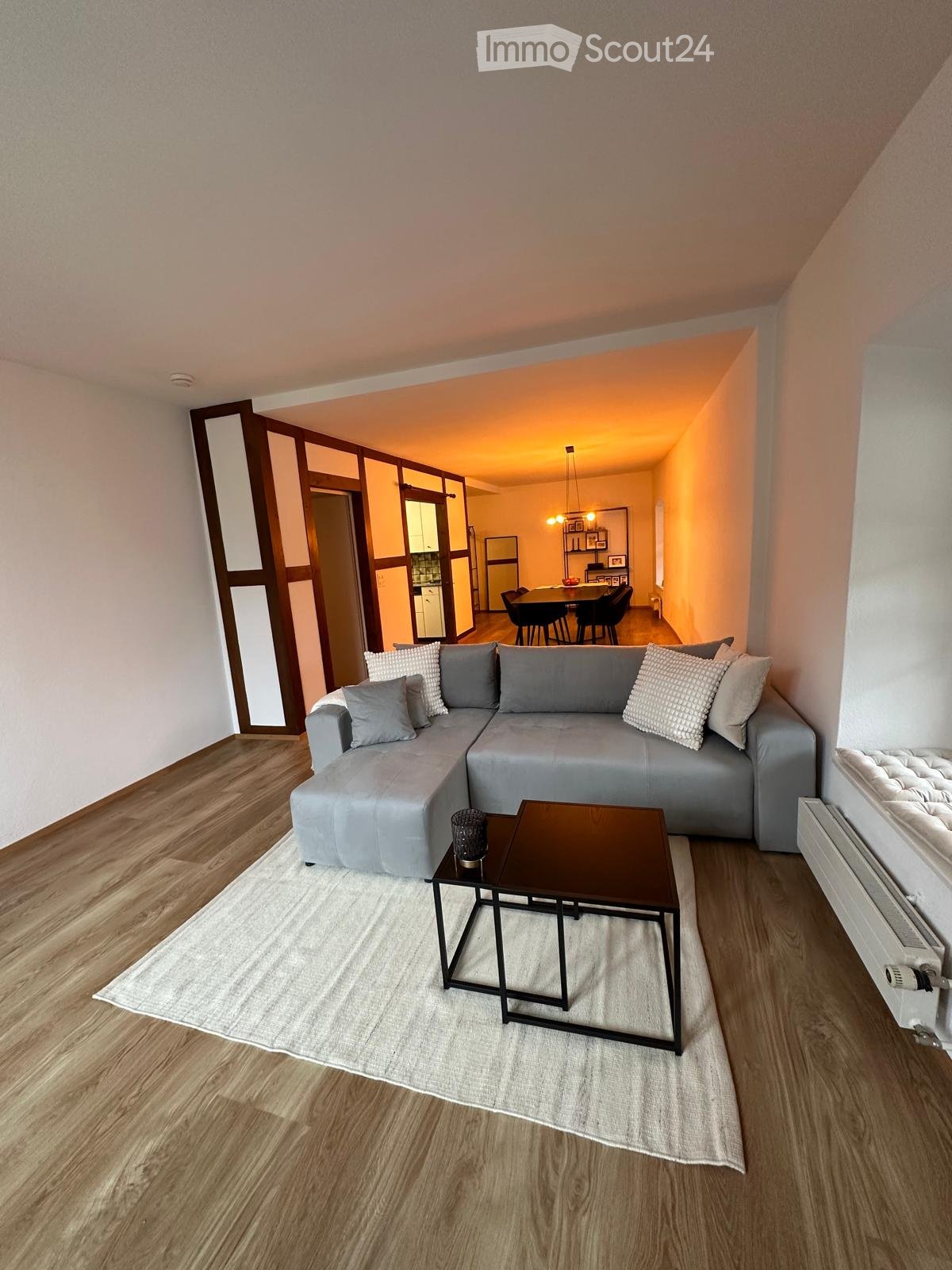 Modern living room with grey sectional sofa, coffee table, dining table, and chairs in the adjacent dining area.