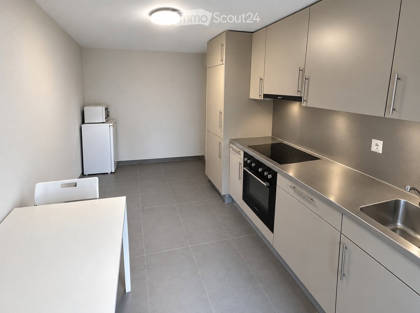 Modern kitchen with light grey cabinets, stainless steel appliances, a white dining table, and a white chair.