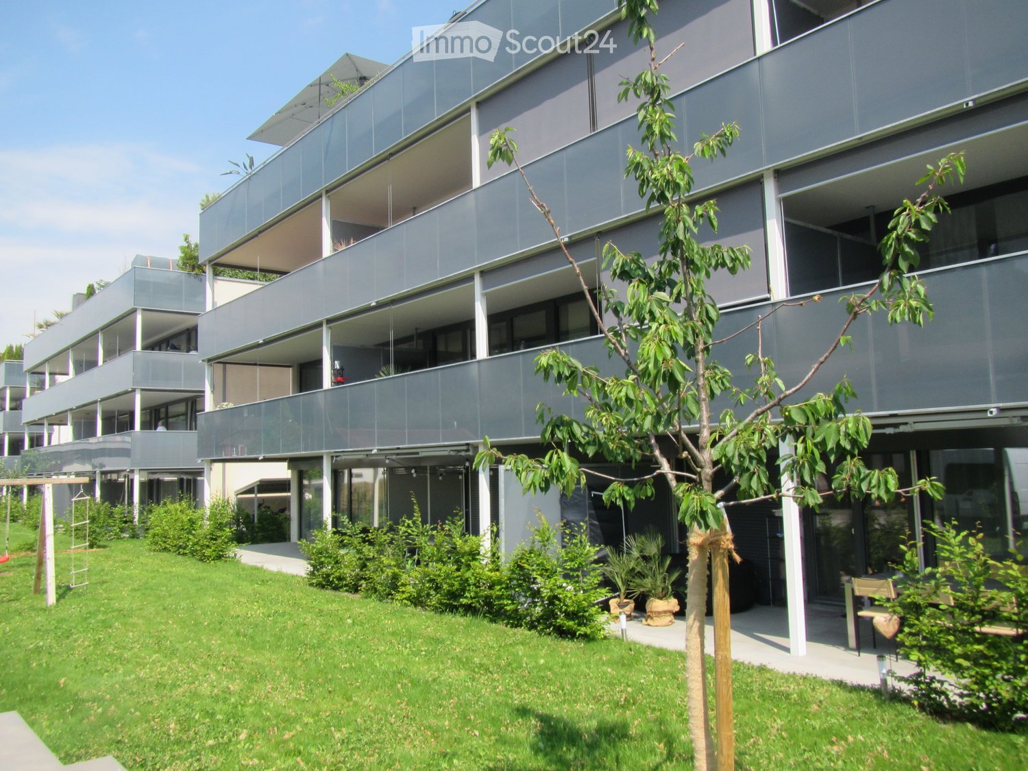 multi-storey building with multiple balconies, large windows, garden, pathway