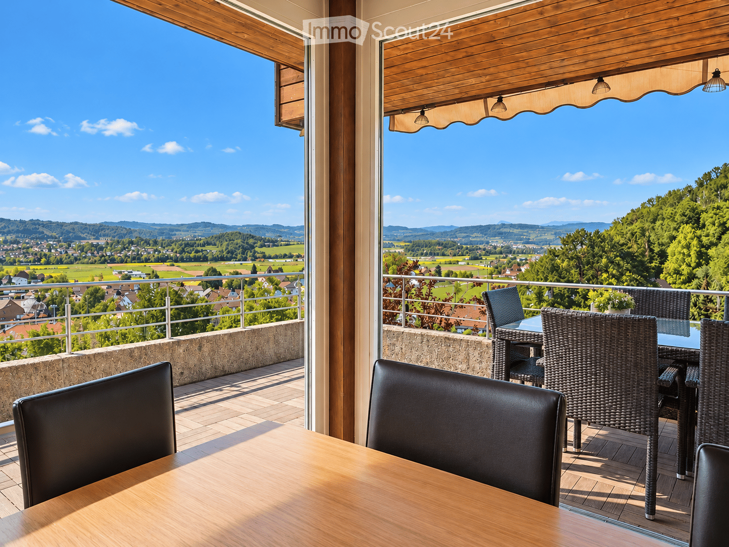 Balcony with wooden decking, outdoor furniture including a table and chairs, overlooking a scenic countryside view.