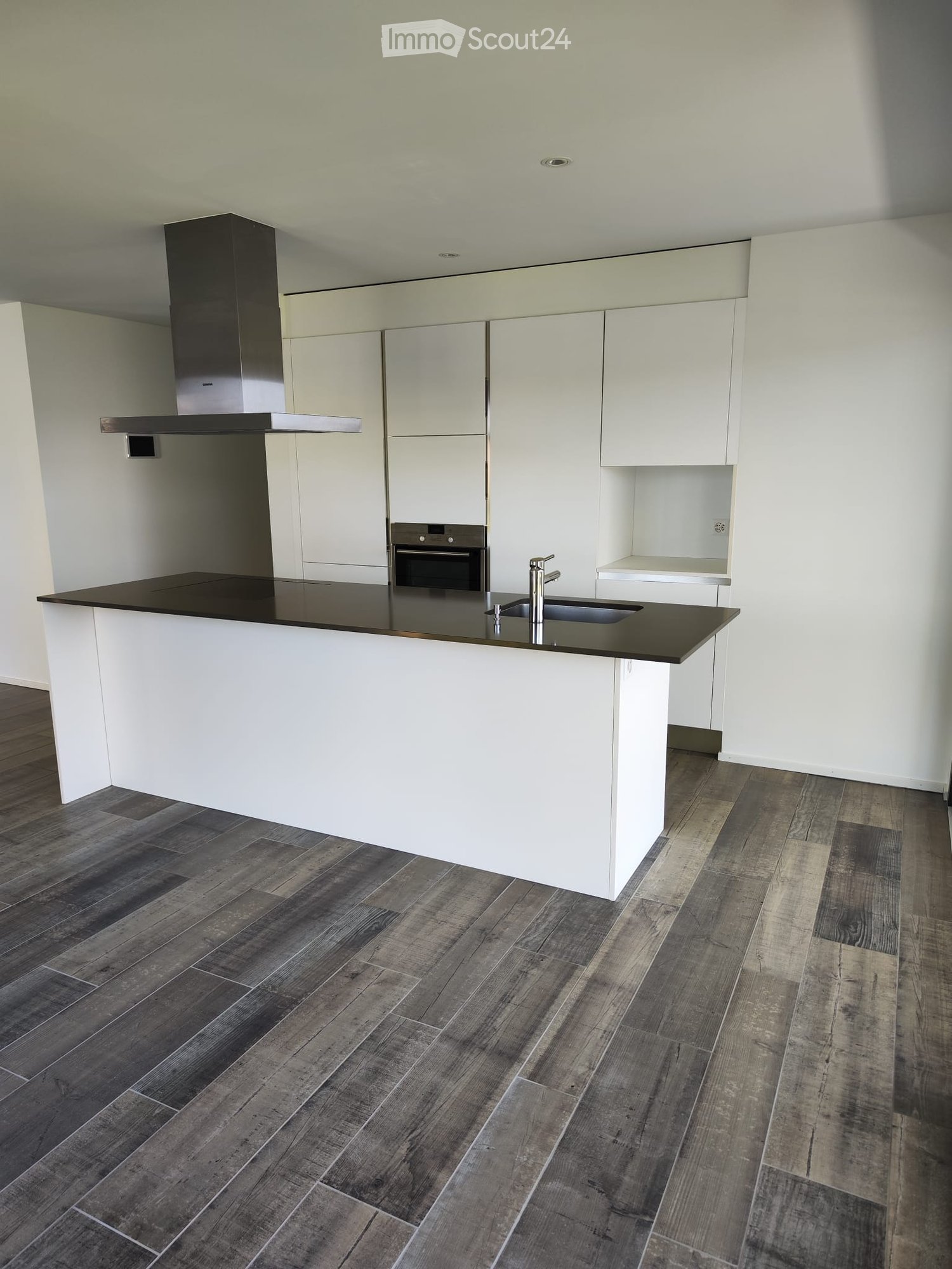 Modern kitchen with white cabinets, dark countertops, and a central island. Features include a stainless steel range hood, built-in oven, and a sink with a modern faucet.