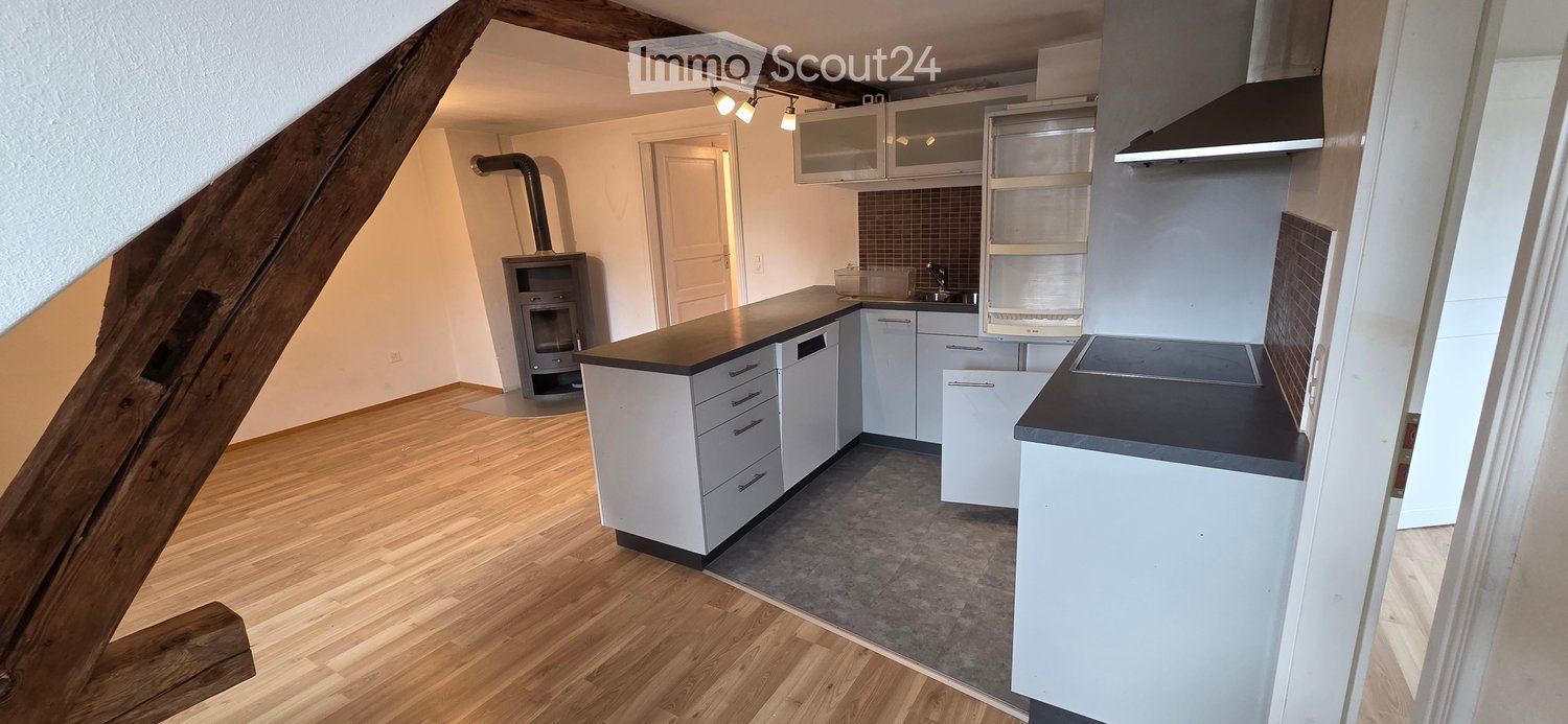 Modern kitchen with white cabinets, black countertops, wooden flooring, and built-in appliances including a dishwasher and range hood.
