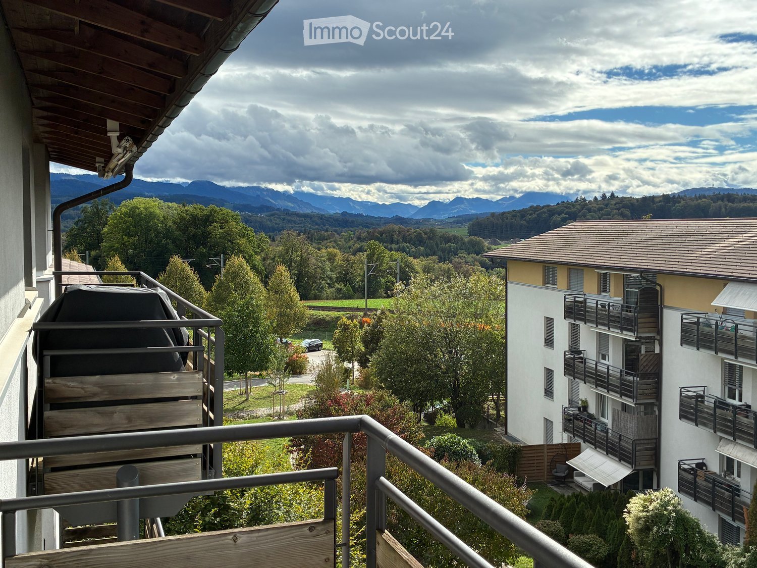 Balcony overlooking a scenic valley with mountains, trees, and neighboring buildings.