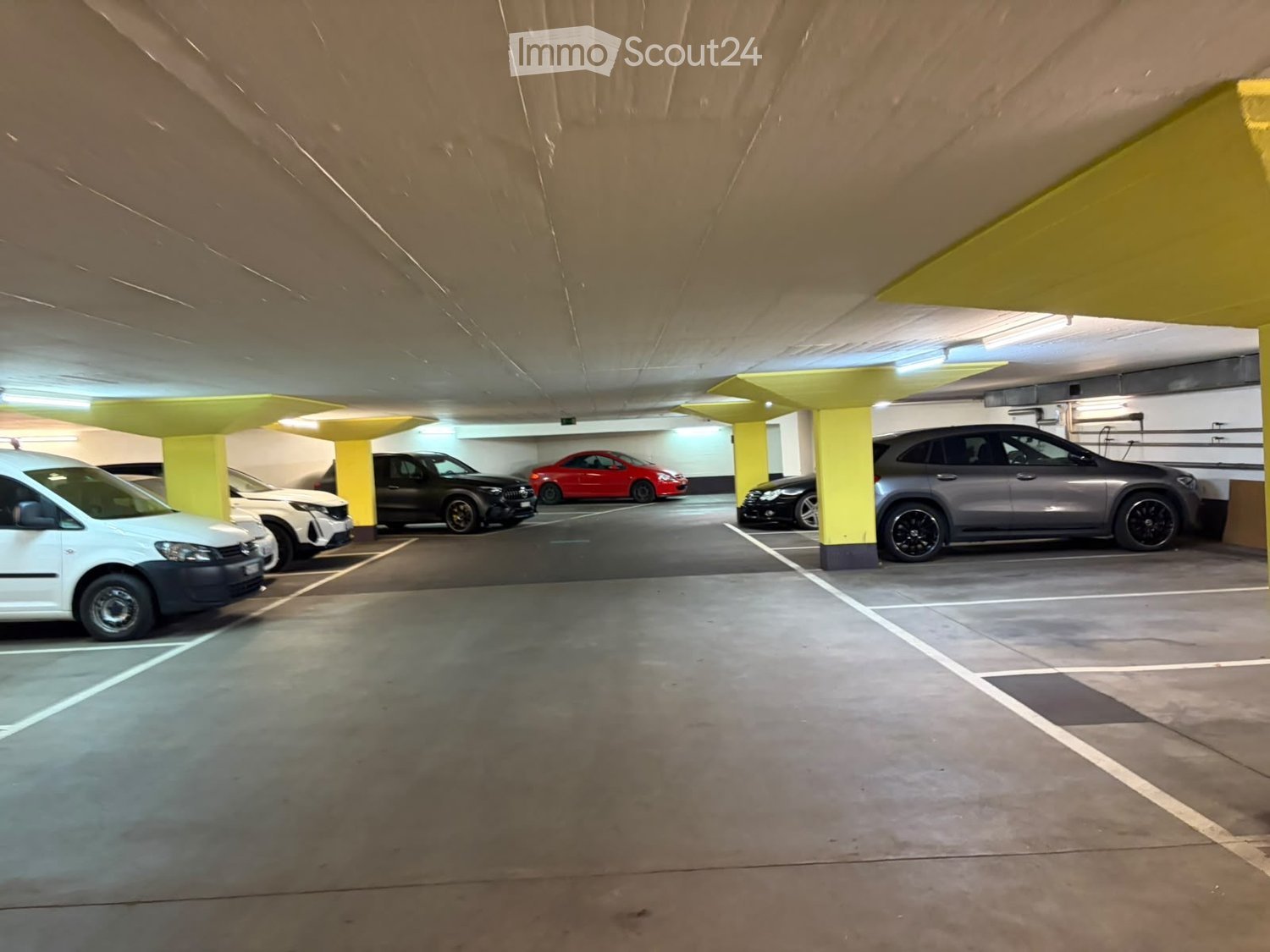 Underground parking area with several parked cars, yellow pillars, and concrete floors.