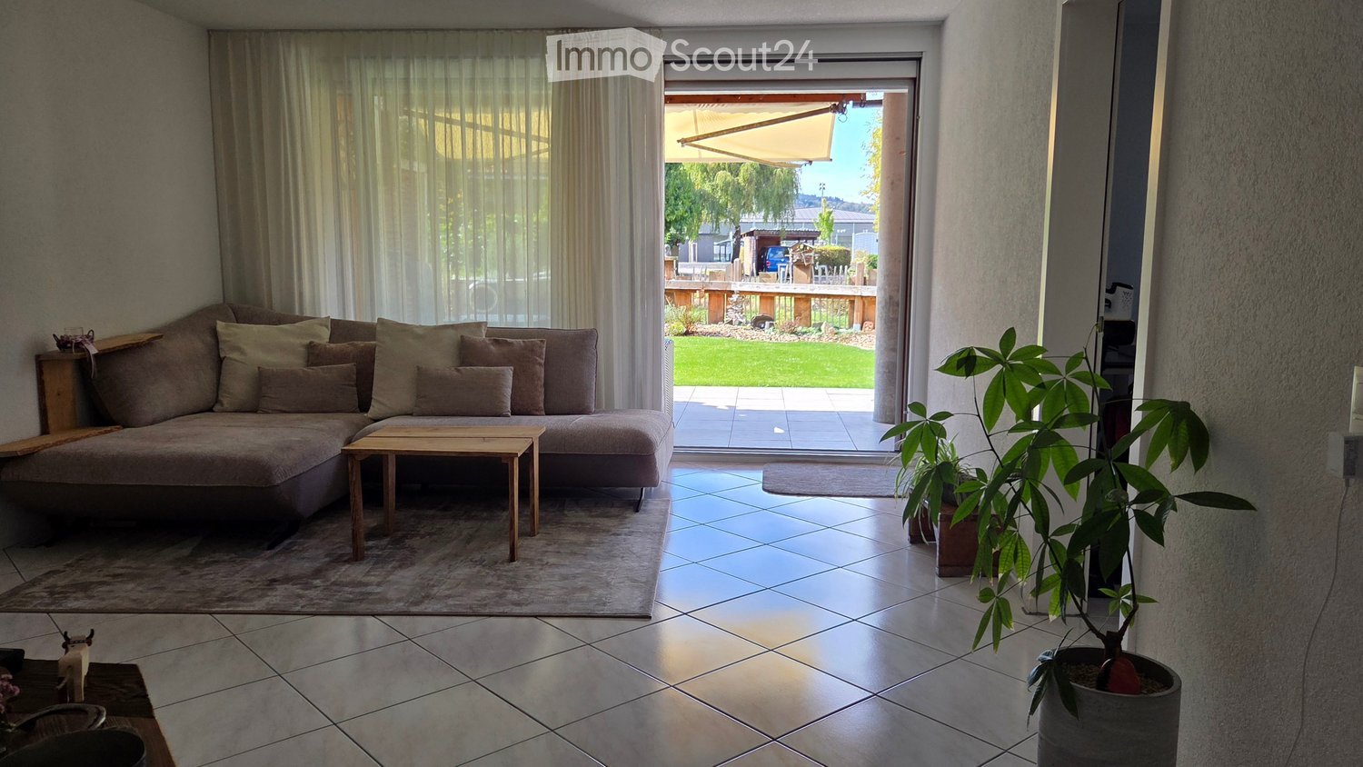 Modern living room with a large sectional sofa, wooden coffee table, side table, and a potted plant near the balcony entrance.