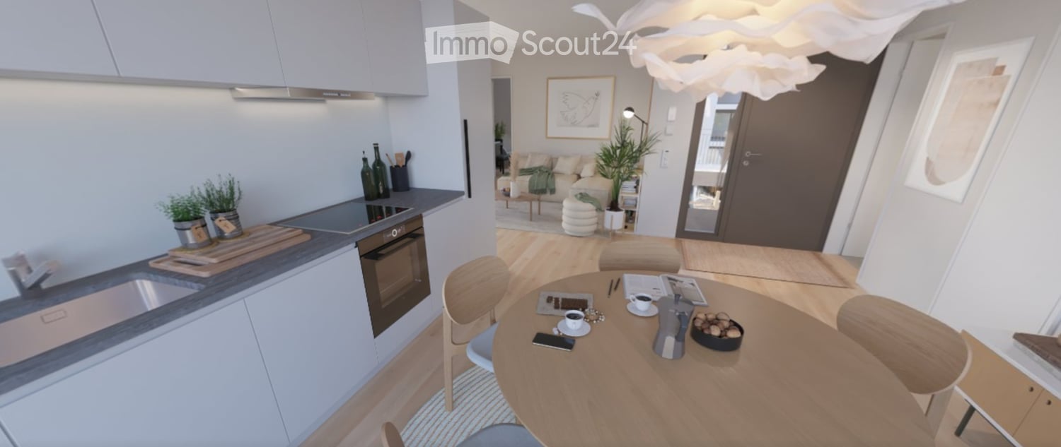 Modern open-plan kitchen and living area with light wood flooring, white cabinets, a round dining table with chairs, a sofa, and decorative plants.