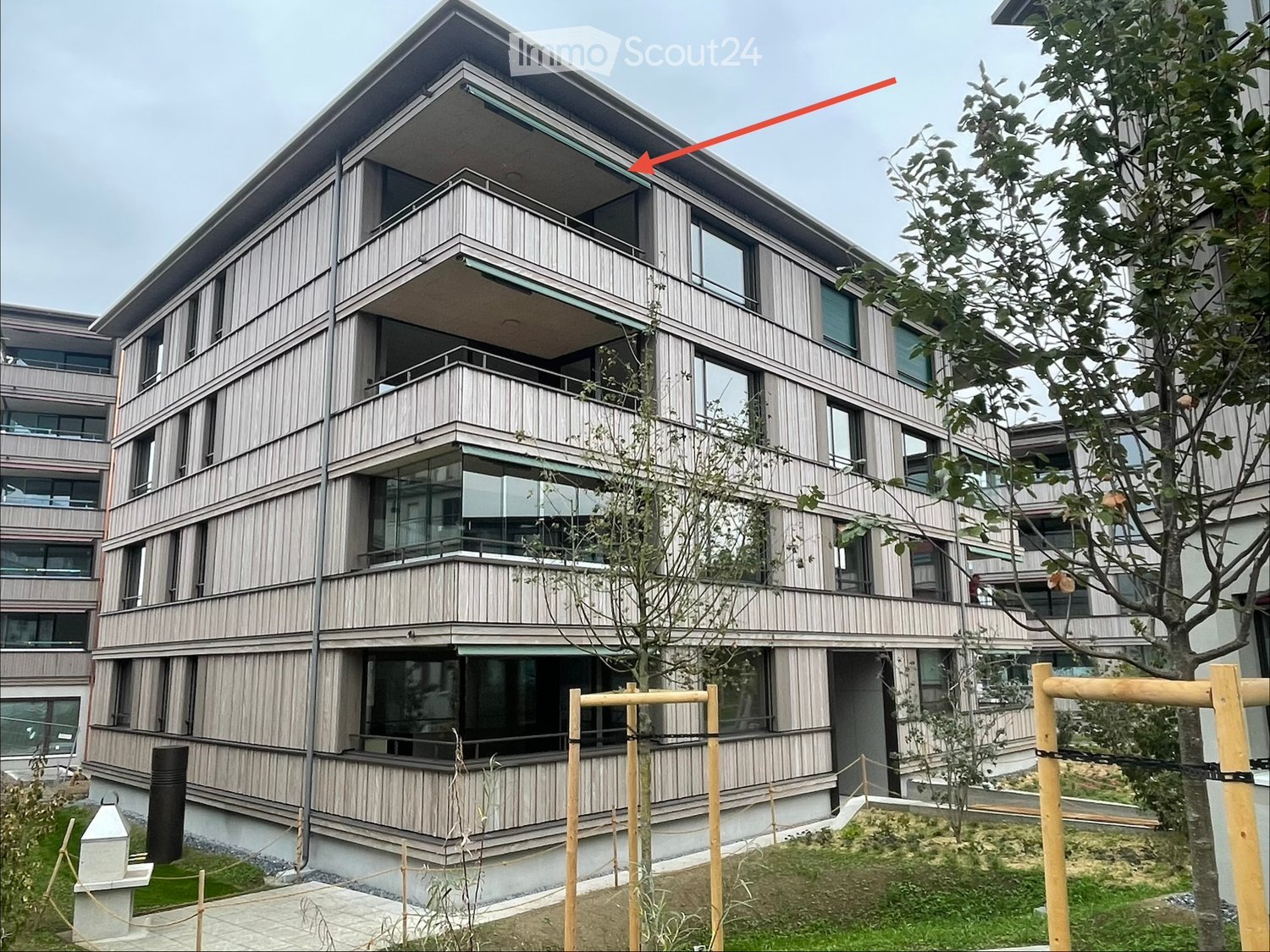 Modern multi-story building with wooden siding, large windows, and balconies. The structure features a contemporary design with clean lines and a raised ground floor.