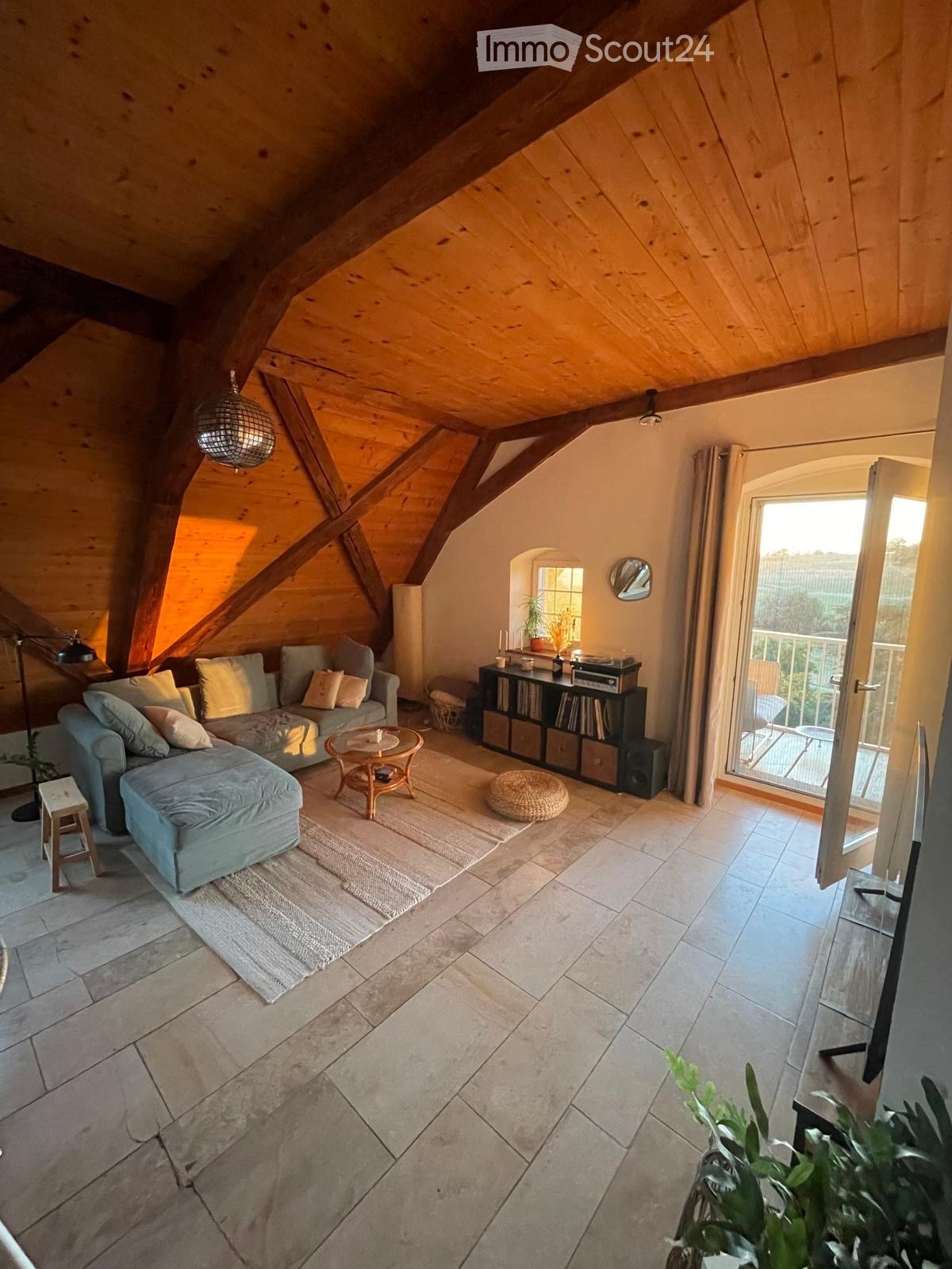 Cozy attic living room with exposed wooden beams, a grey sectional sofa, a round coffee table, a bookshelf, and a balcony access.