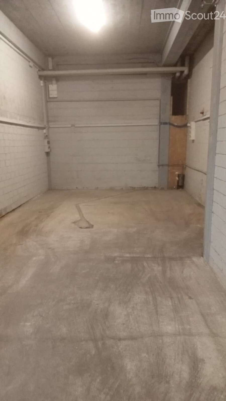Empty garage with concrete floor, brick walls, and a large closed garage door. No furniture or equipment present.
