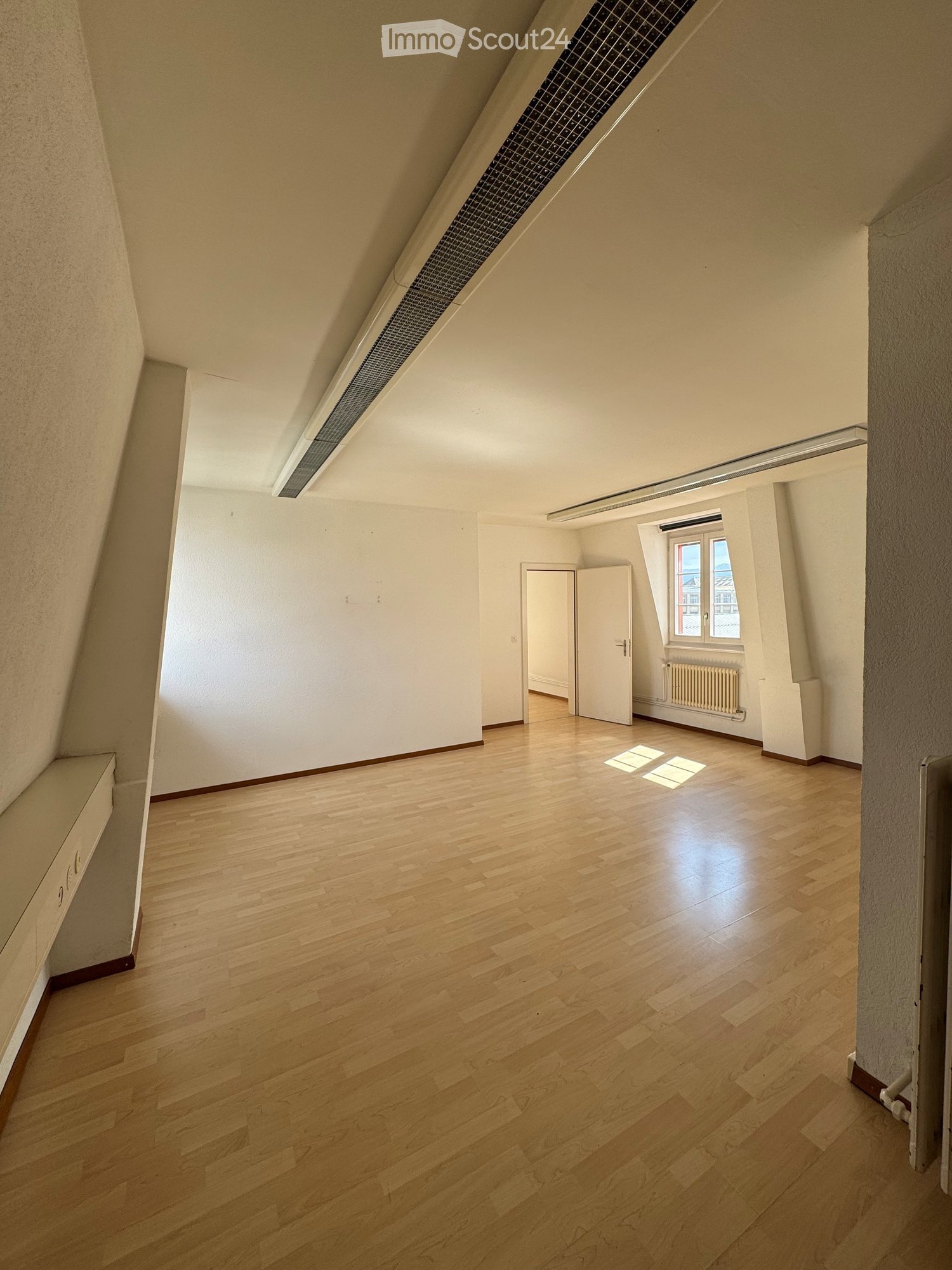 Empty attic room with wooden flooring, white walls, and a skylight window. The space features a slanted ceiling and a small window with a view.