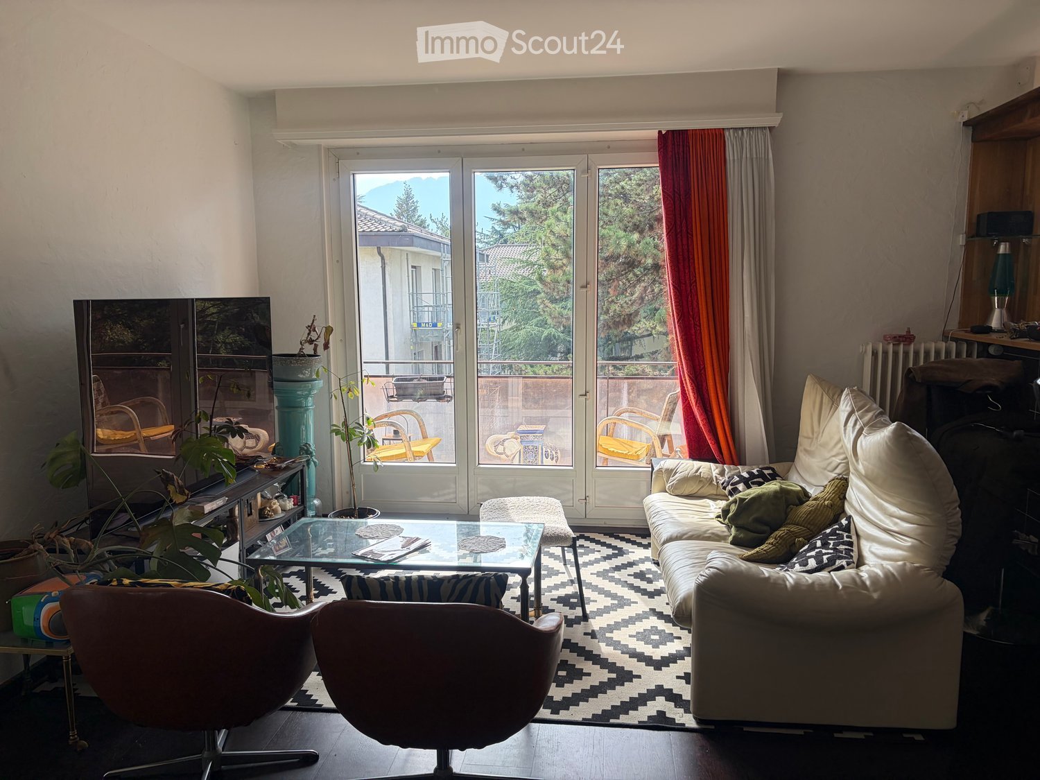 Living room with a large window offering a view, a sofa, coffee table, chairs, and plants.