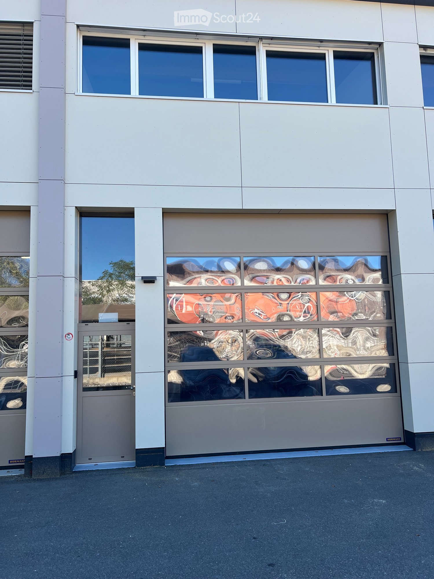 Modern building facade with large windows and a garage door featuring abstract glass panels.