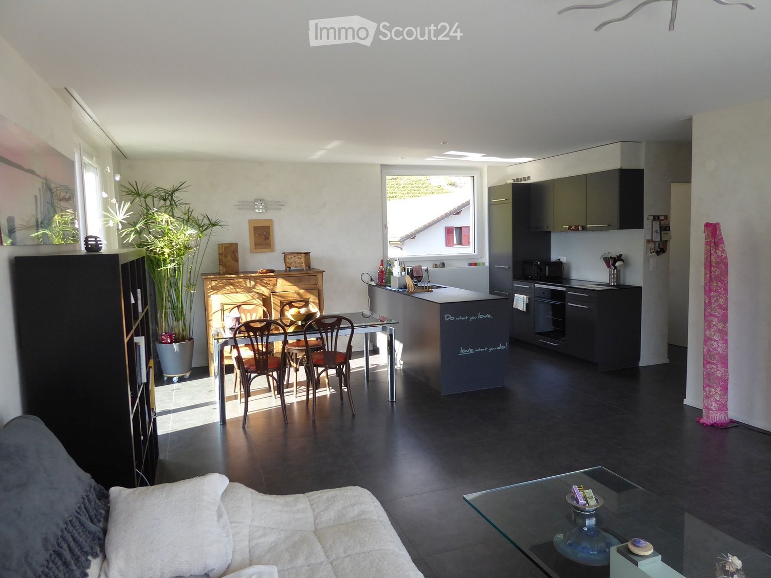 Open-plan living and dining area with a modern kitchen, featuring a sofa, coffee table, dining table with chairs, kitchen island, and various appliances.