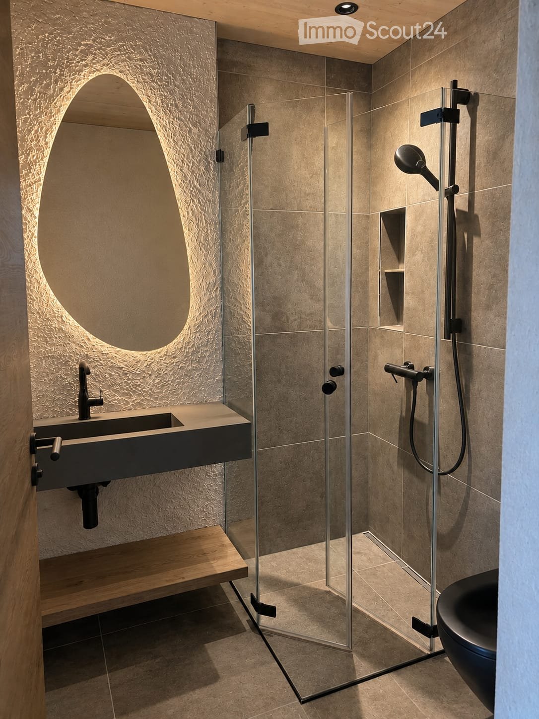 Modern bathroom with a sleek sink, glass-enclosed shower, and a dark-toned bathtub. Features include a textured wall, a built-in wooden shelf, and a large, curved mirror.