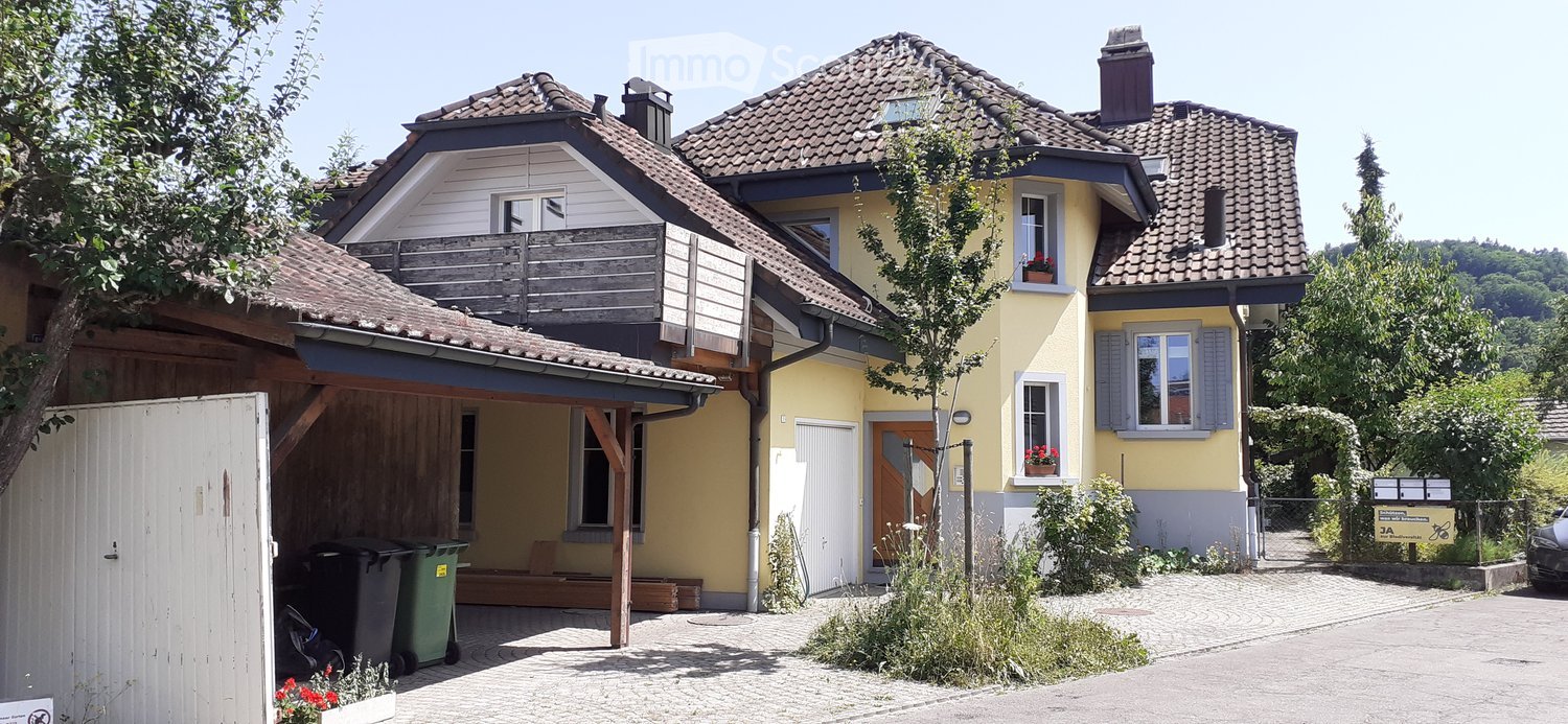 Two-story house with yellow exterior, tiled roof, garage, balcony, and small garden area.