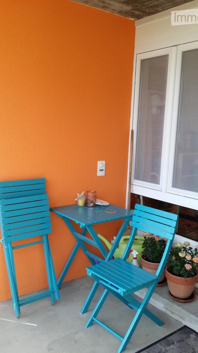 Balcony with two turquoise folding chairs, small table, potted plants, and a spray bottle on the floor.