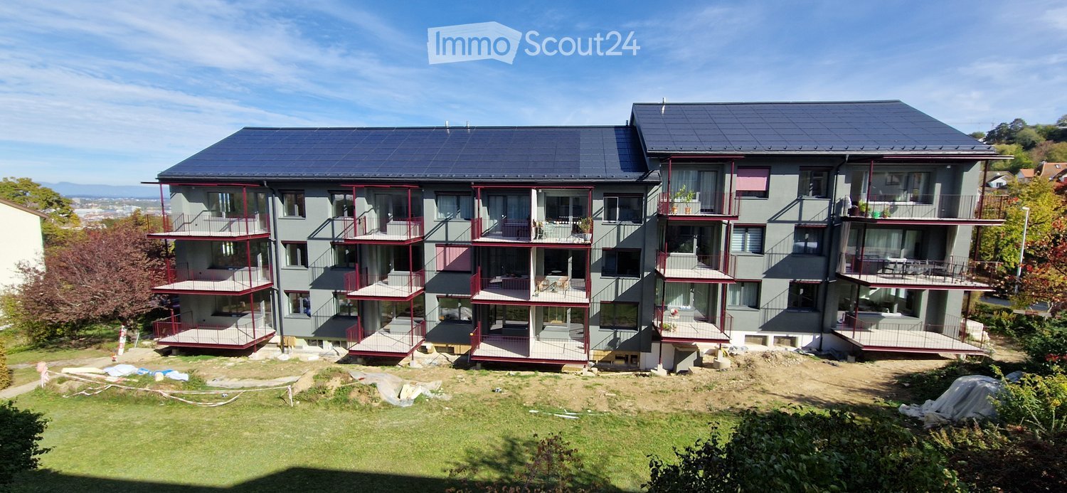 Modern multi-story residential building with solar panels on the roof, balconies, and surrounding greenery.