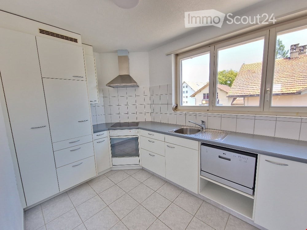 Modern kitchen with white cabinets, stainless steel appliances, and large windows overlooking a residential area.