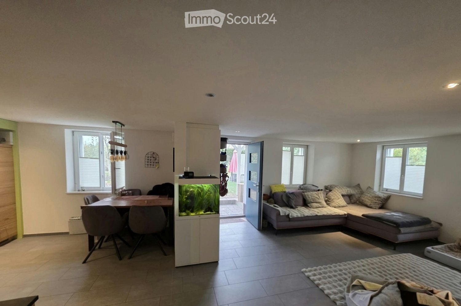 Modern living and dining area with a sectional sofa, dining table with chairs, fish tank, and decorative pillows.