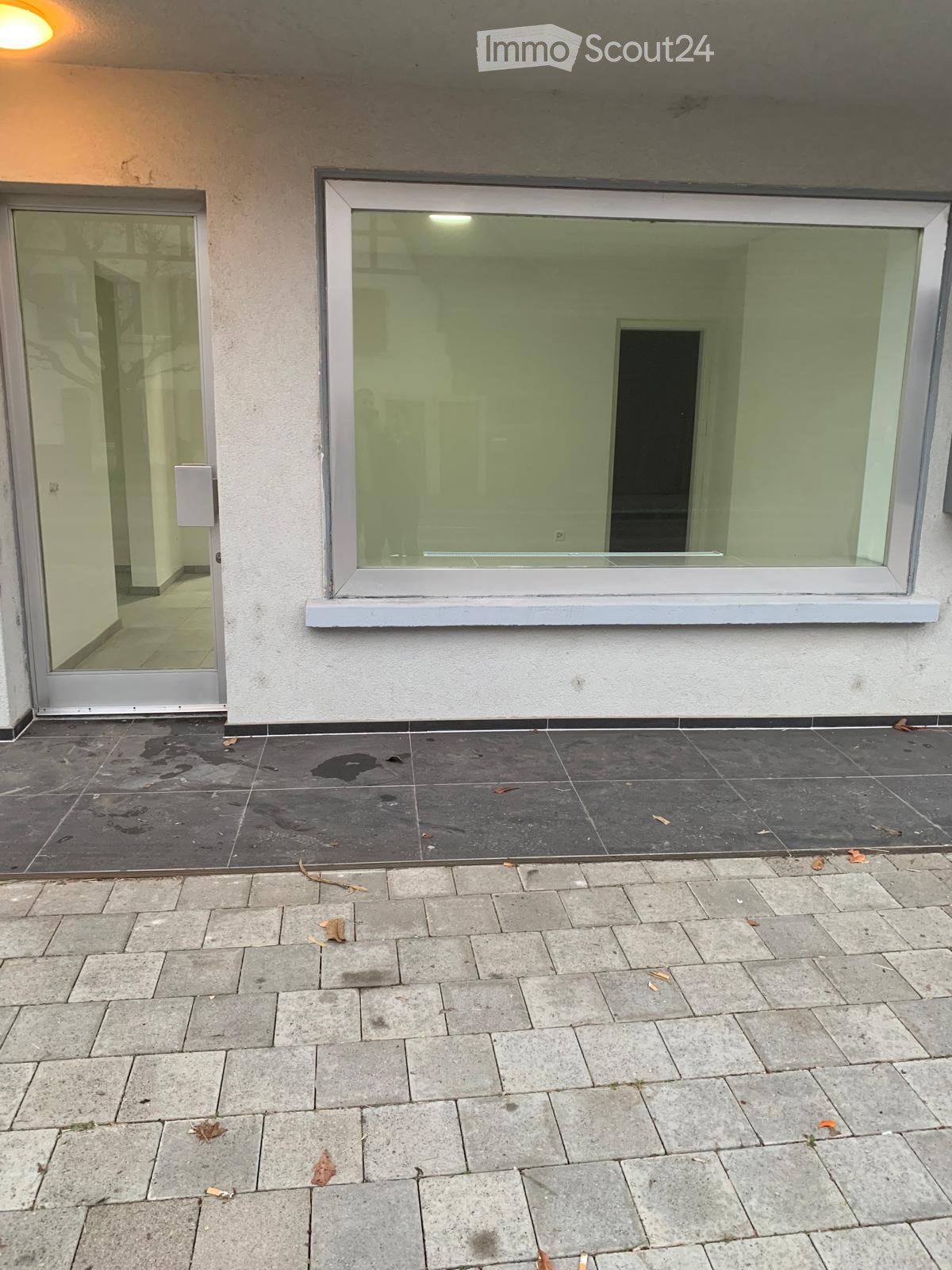 Empty balcony area with tiled flooring, a large window, and a glass door leading to an interior space.