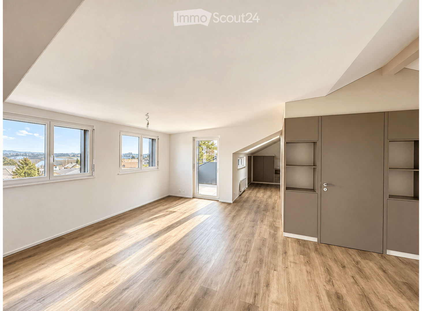 Empty attic room with wooden flooring, white walls, large windows, and built-in closet units.