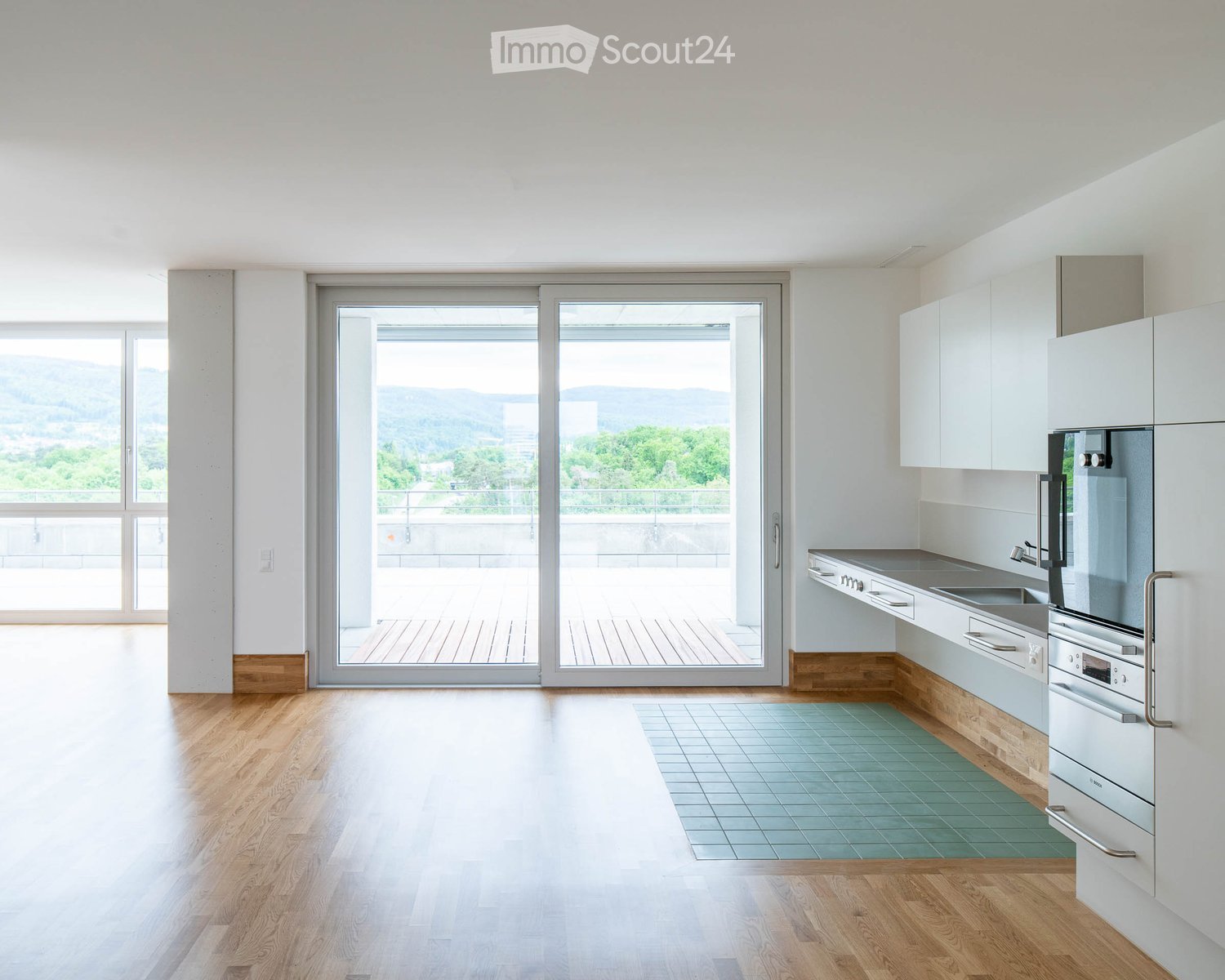Modern kitchen with white cabinets, stainless steel appliances, wooden flooring, and large windows offering a scenic view.