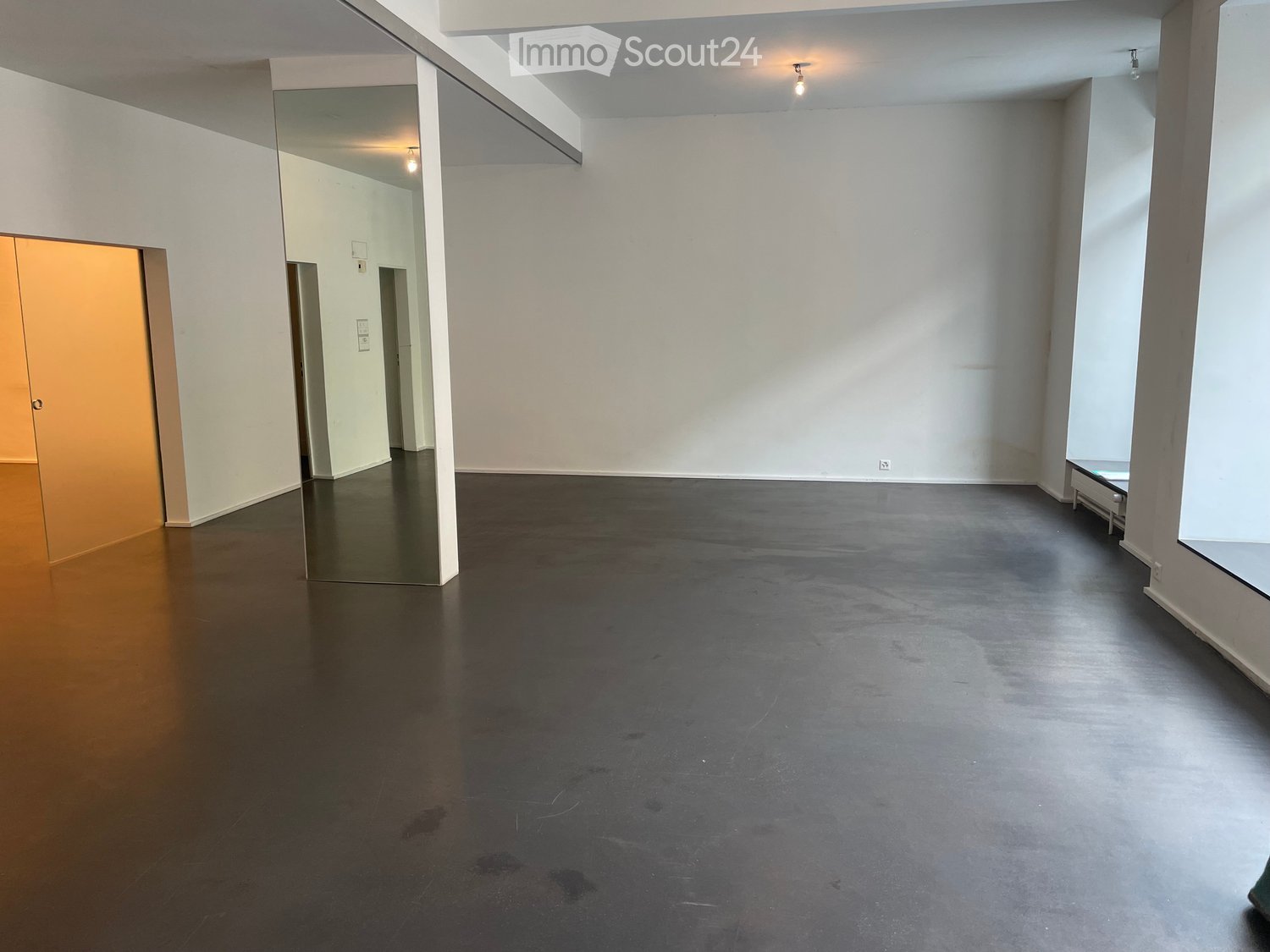 Empty room with white walls, dark polished concrete floor, and large windows. No furniture or equipment present.