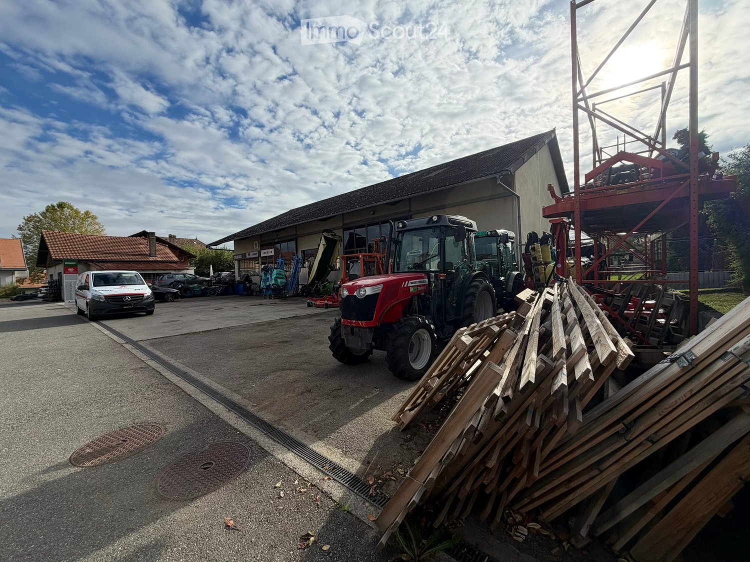 A commercial building with a large garage area, featuring a red tractor, a white van, and various construction materials and equipment.