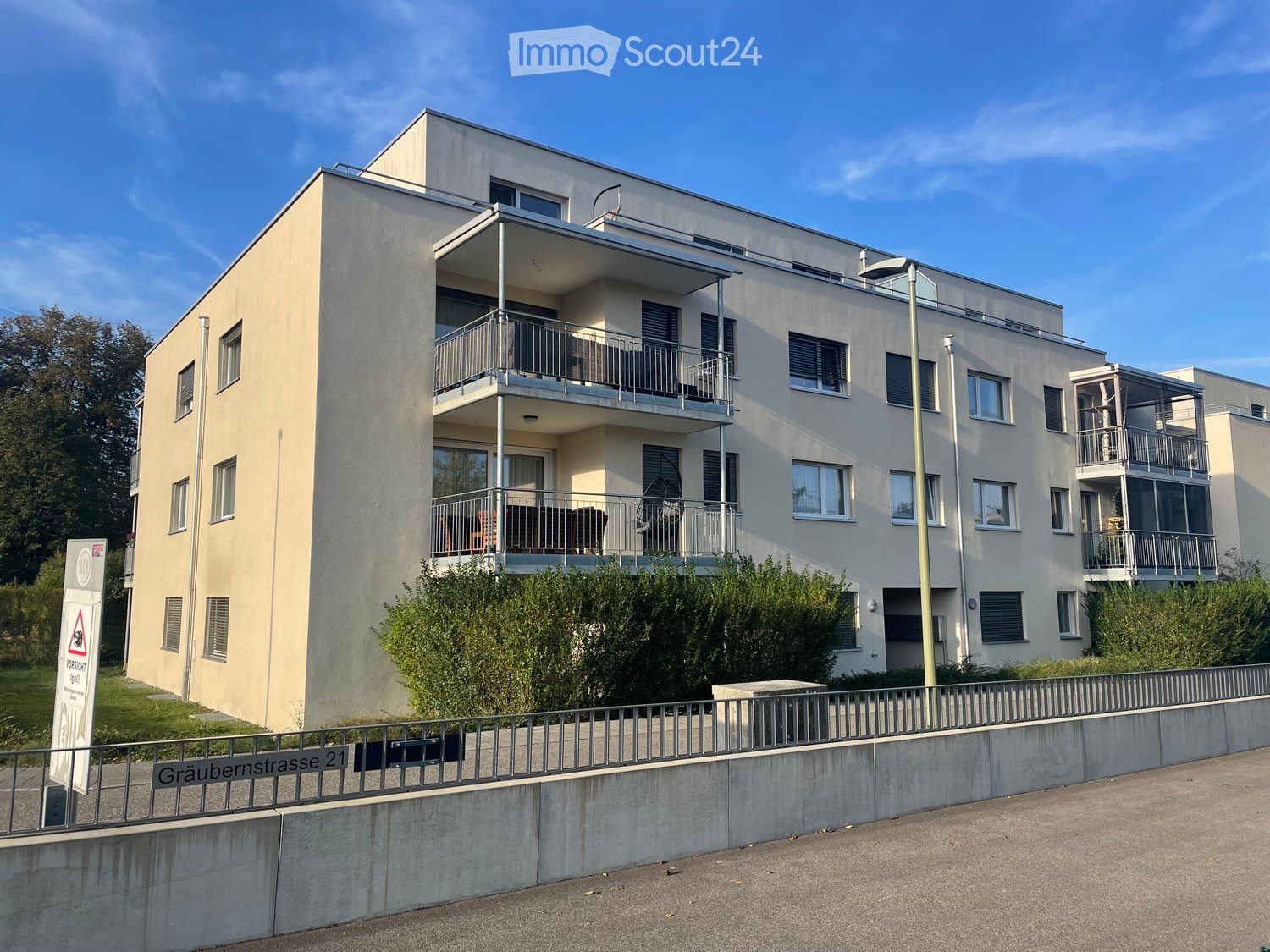 Modern multi-story residential building with balconies, large windows, and a clean facade.