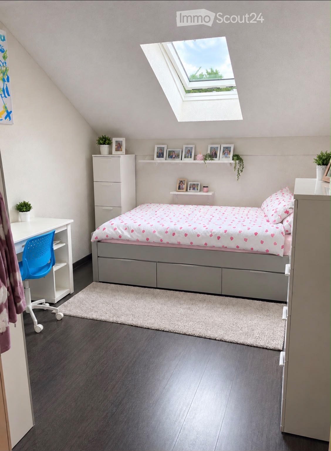 Cozy bedroom with a bed, desk, chair, and shelves. Features a skylight window, grey flooring, and decorative picture frames on the wall.