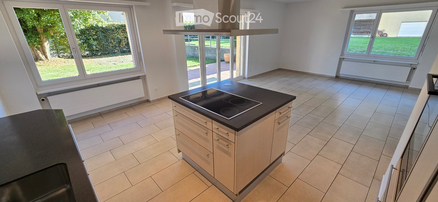 Modern kitchen with light-colored cabinets, a black countertop, and an induction stove. Large windows provide natural light and a view of the garden.