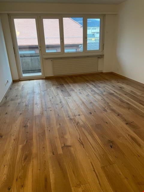 Empty room with wooden flooring, large windows, and white walls. No furniture or equipment present.