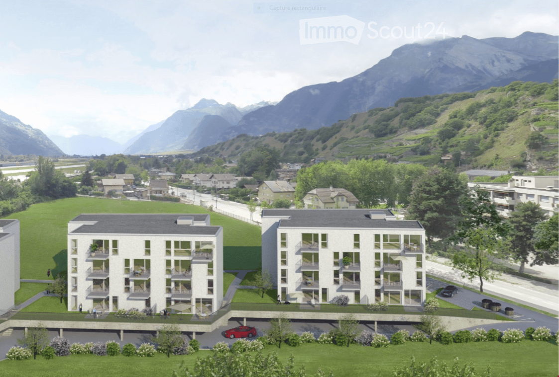 Modern multi-story residential building with balconies and parking area, surrounded by green landscape and mountains.