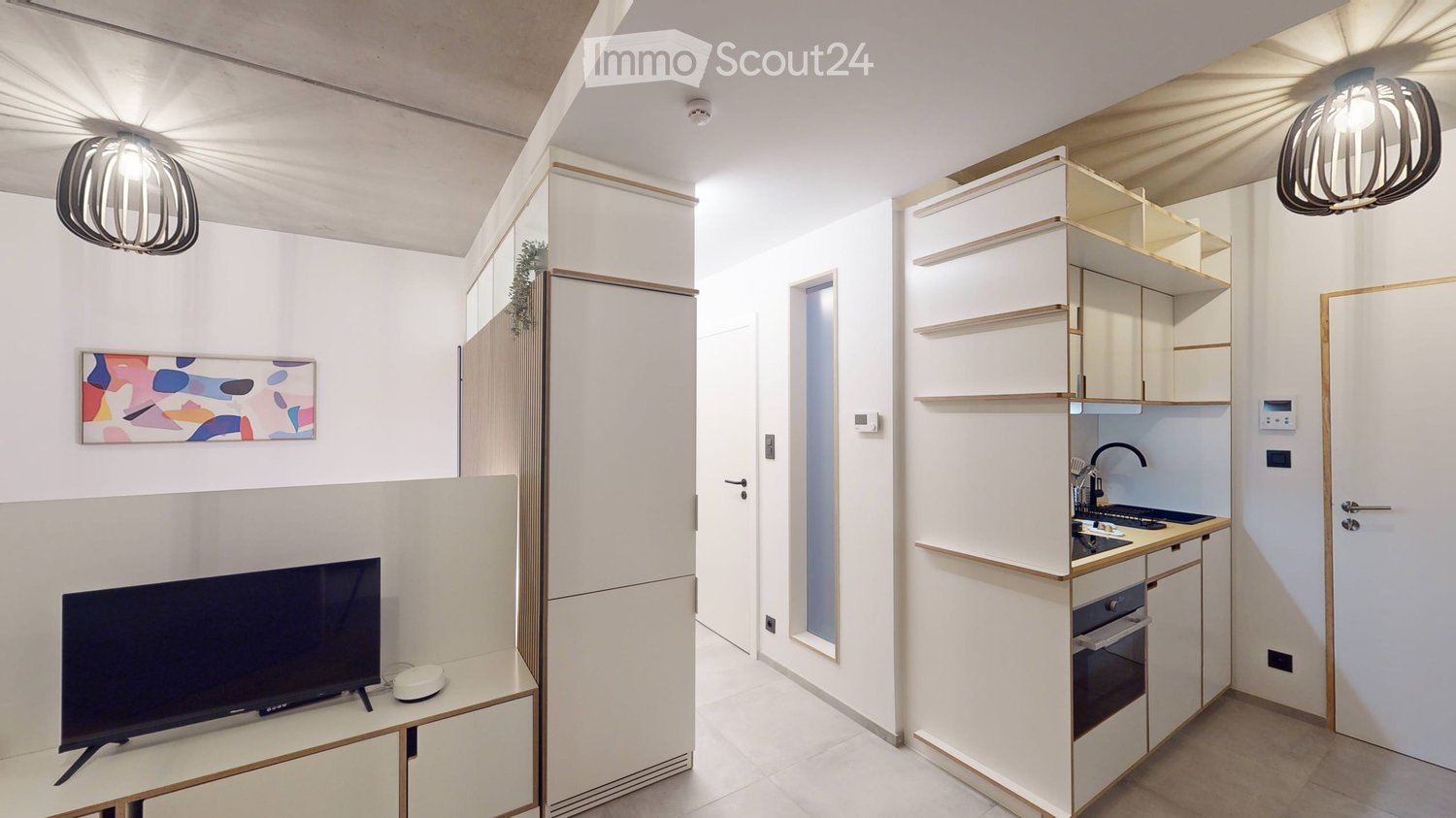 Modern, compact living space with a TV, small kitchen area, and built-in storage cabinets.