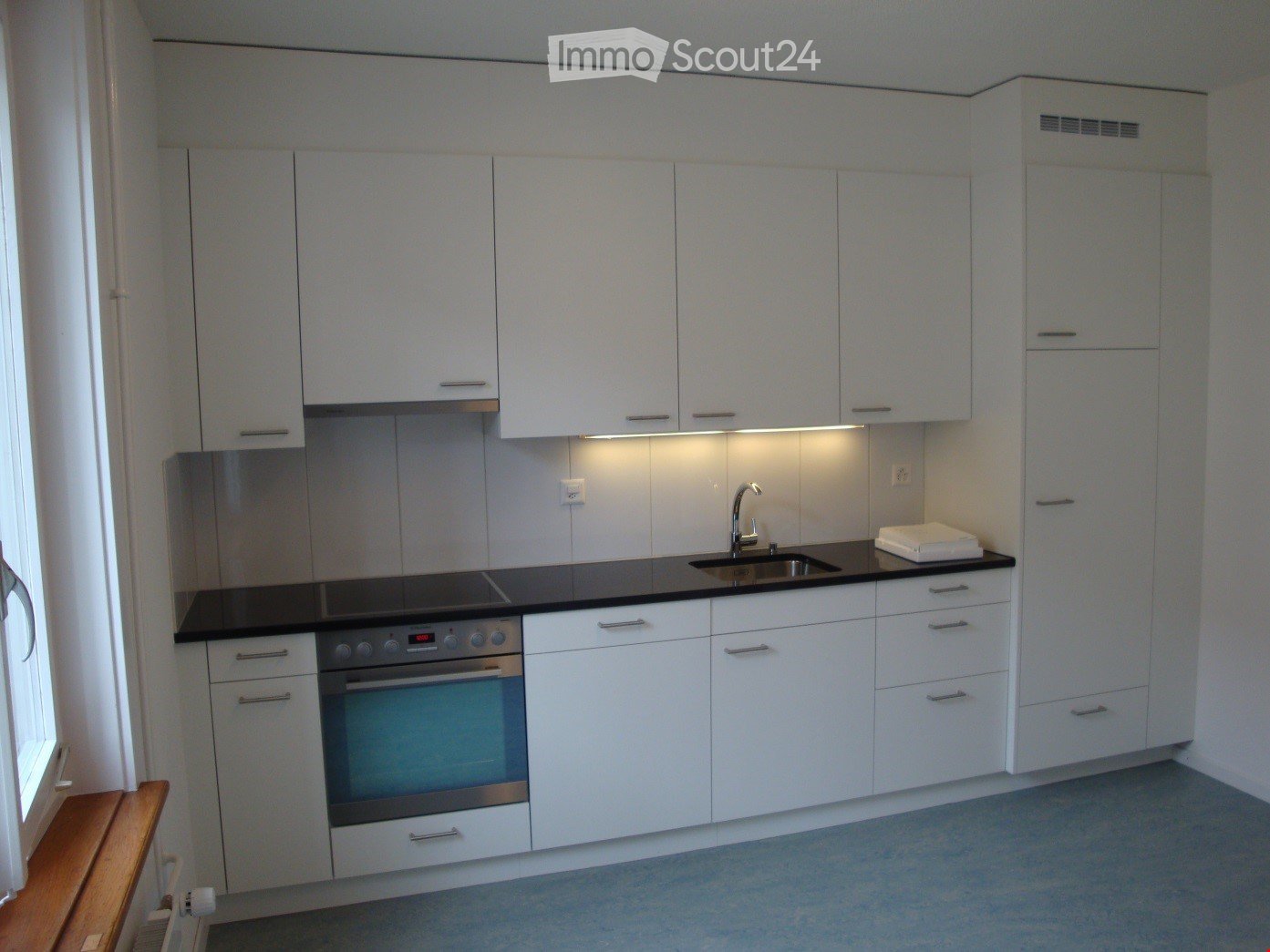 Modern kitchen with white cabinets, black countertop, stainless steel oven, sink, and faucet. Features built-in lighting and a small towel on the counter.
