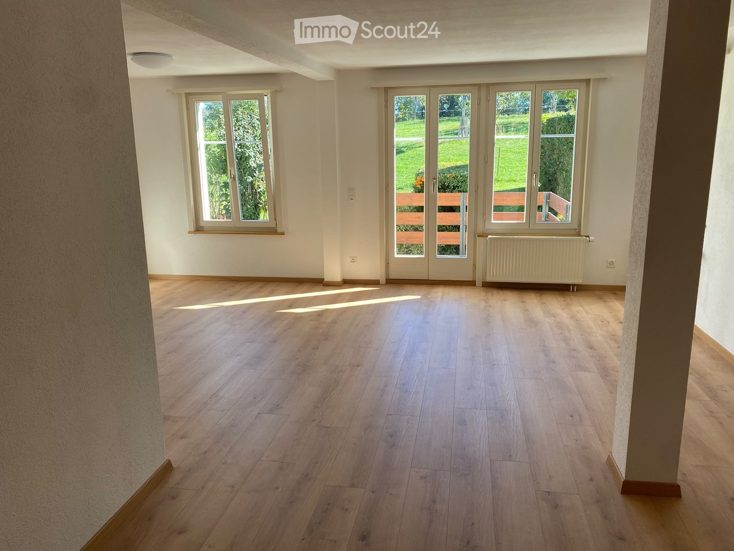 Empty room with wooden flooring, large windows, and a radiator. No furniture or equipment present.
