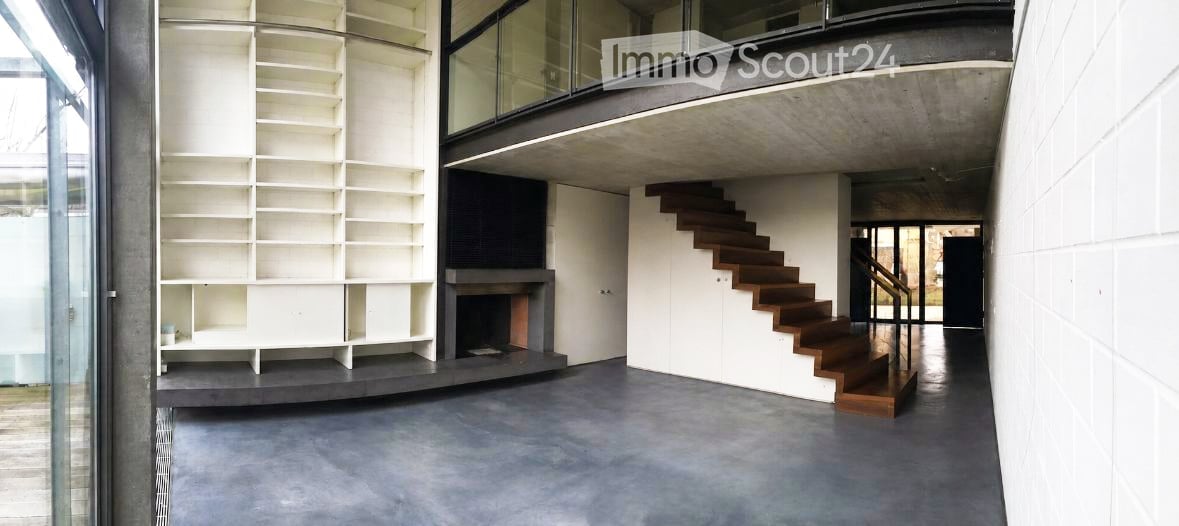 Modern interior with a large open space, featuring a built-in bookshelf, a fireplace, and a wooden staircase leading to an upper level.