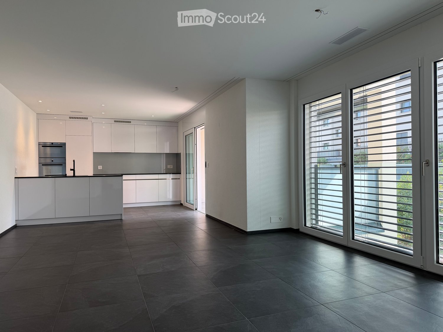 Modern kitchen with white cabinets, stainless steel appliances, dark tiled floor, and large sliding glass doors leading to a balcony.