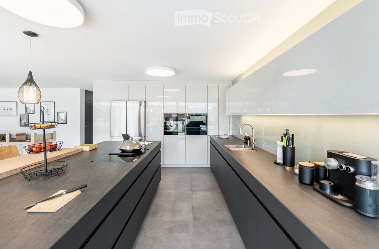 Modern kitchen with white cabinets, stainless steel appliances, and a central island. Features include a coffee maker, knife block, pendant lighting, and a fruit basket on the counter.