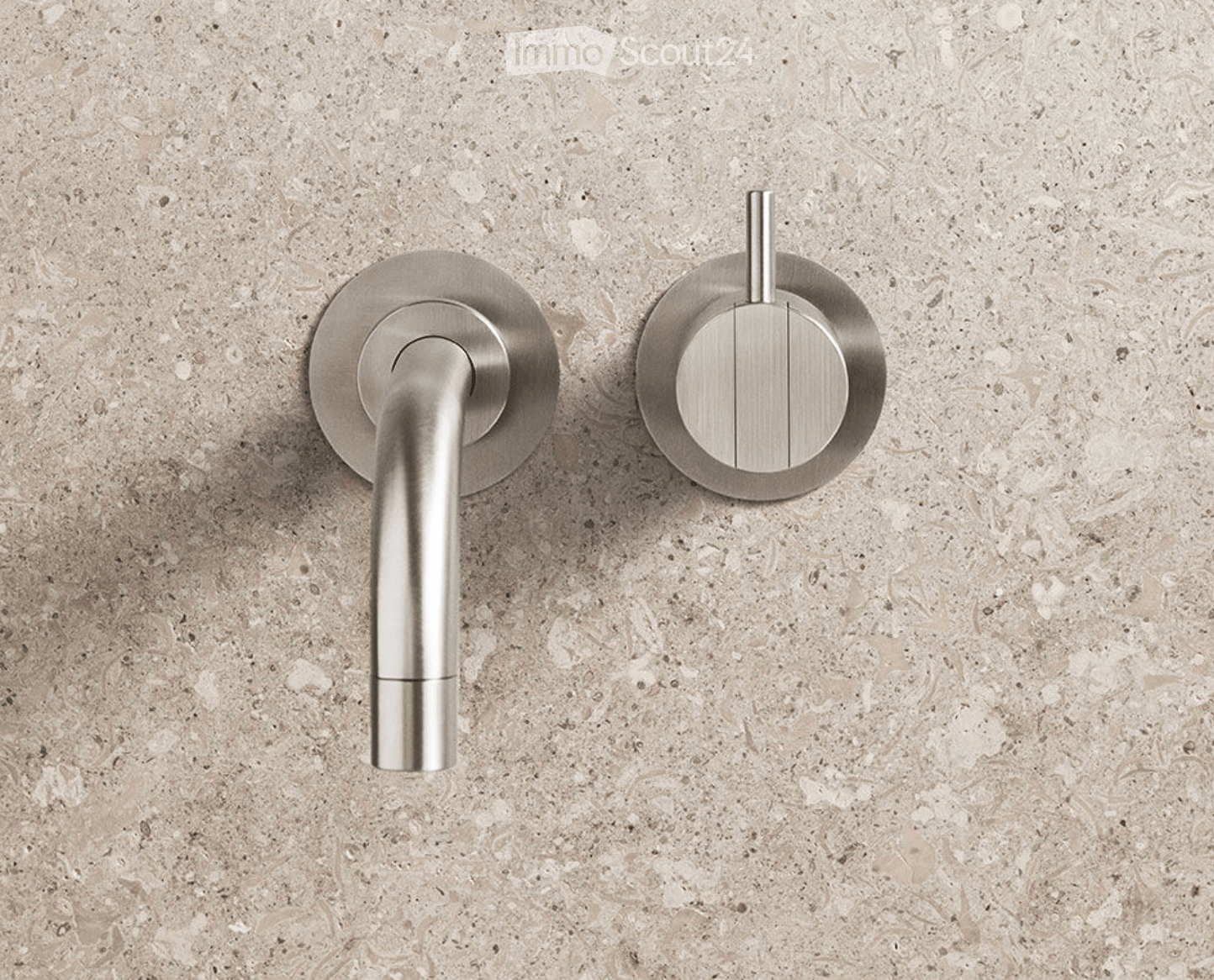 Modern bathroom fixtures featuring a sleek chrome faucet and a round shower handle mounted on a textured beige tile wall.
