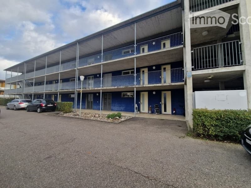 Multi-story apartment building with blue exterior, balconies, and parking area.