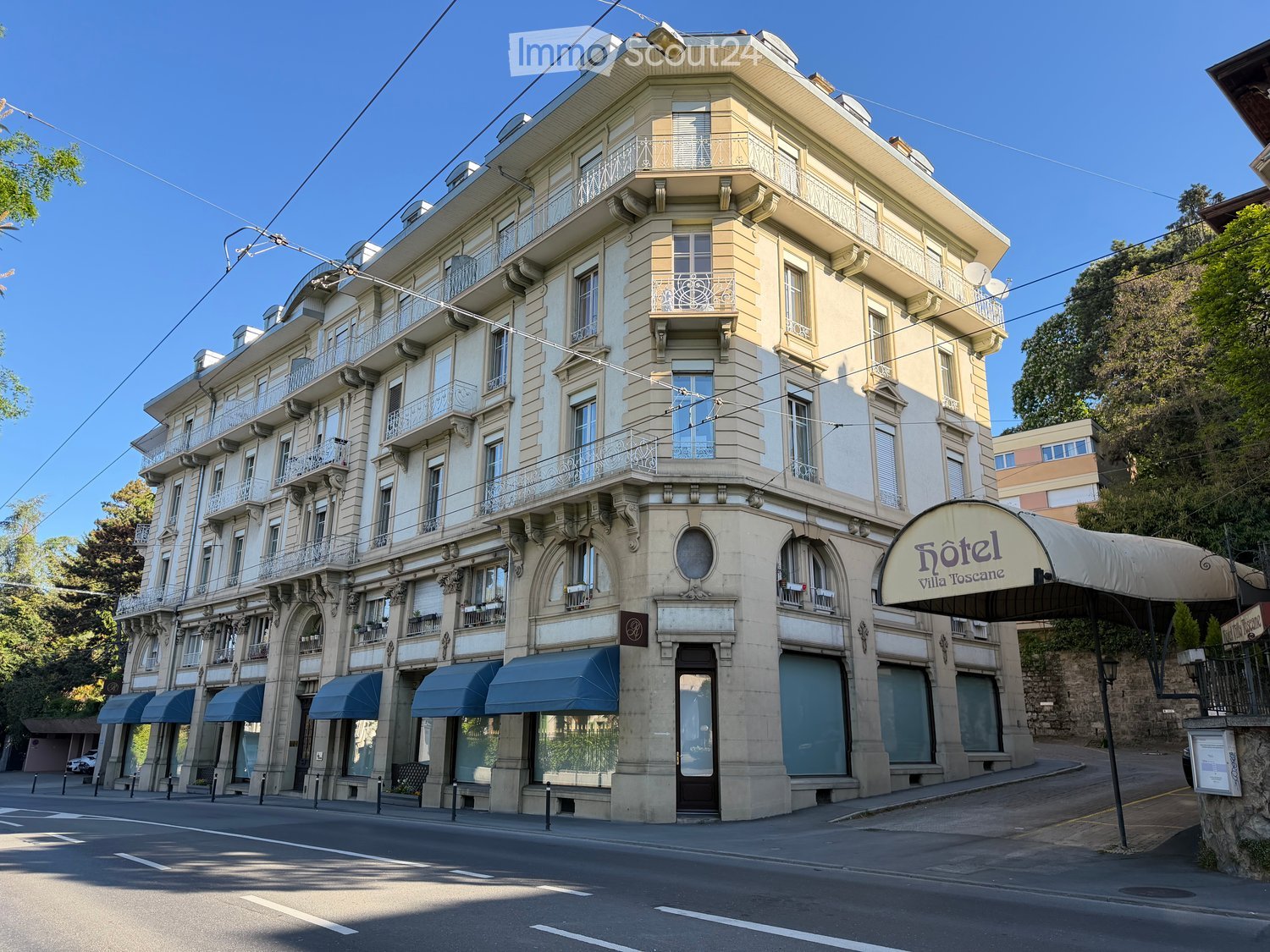 A multi-story building with classical architecture, featuring arched windows, balconies, and a sign reading "Hôtel Villa Toscana".