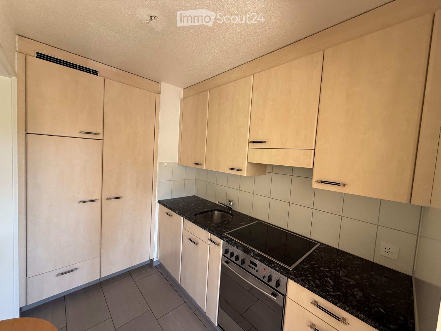 Modern kitchen with light-colored cabinets, granite countertop, sink, electric stove, and oven.