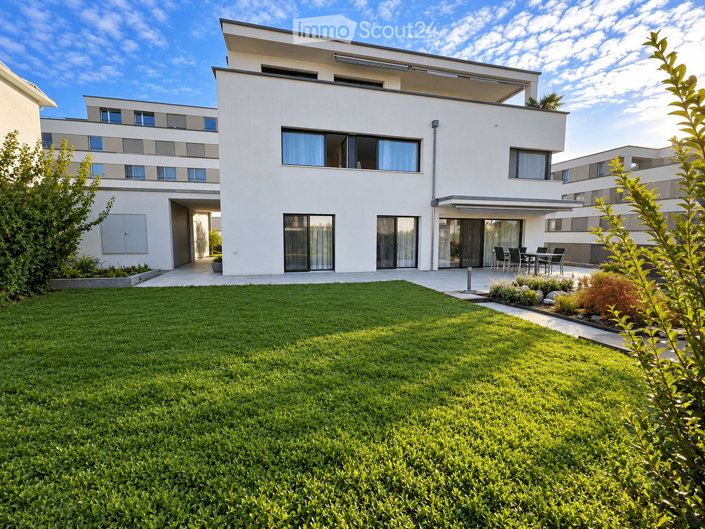 Modern two-story house with white exterior, large windows, and a well-maintained lawn in front.