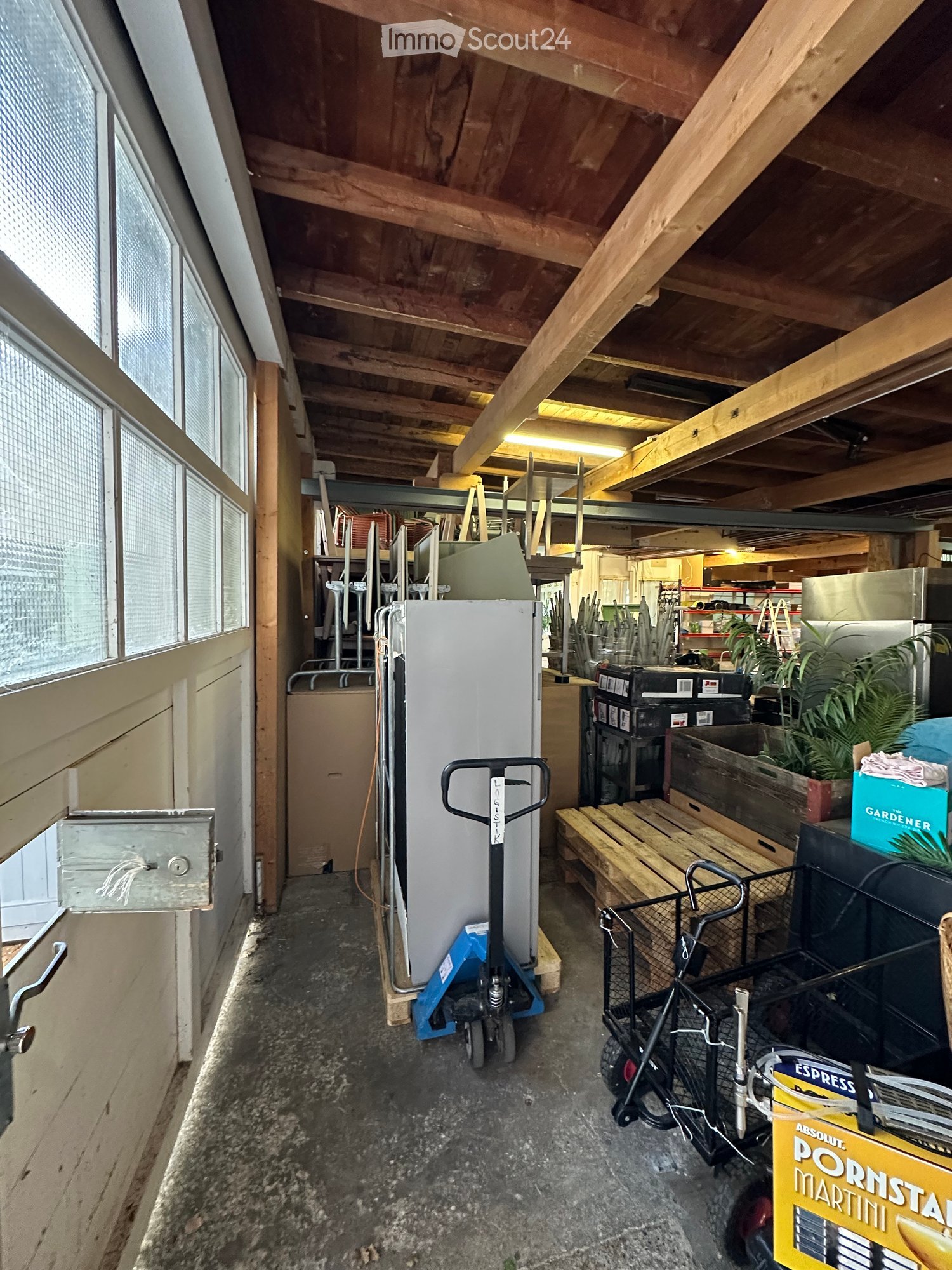 The image shows a cluttered storage area with a refrigerator, hand truck, cart, bench, potted plants, ladder, and storage boxes.