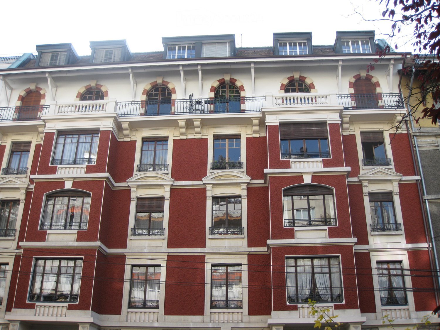 Multi-story residential building with red brick facade, white decorative trim, arched windows, and balconies with metal railings.