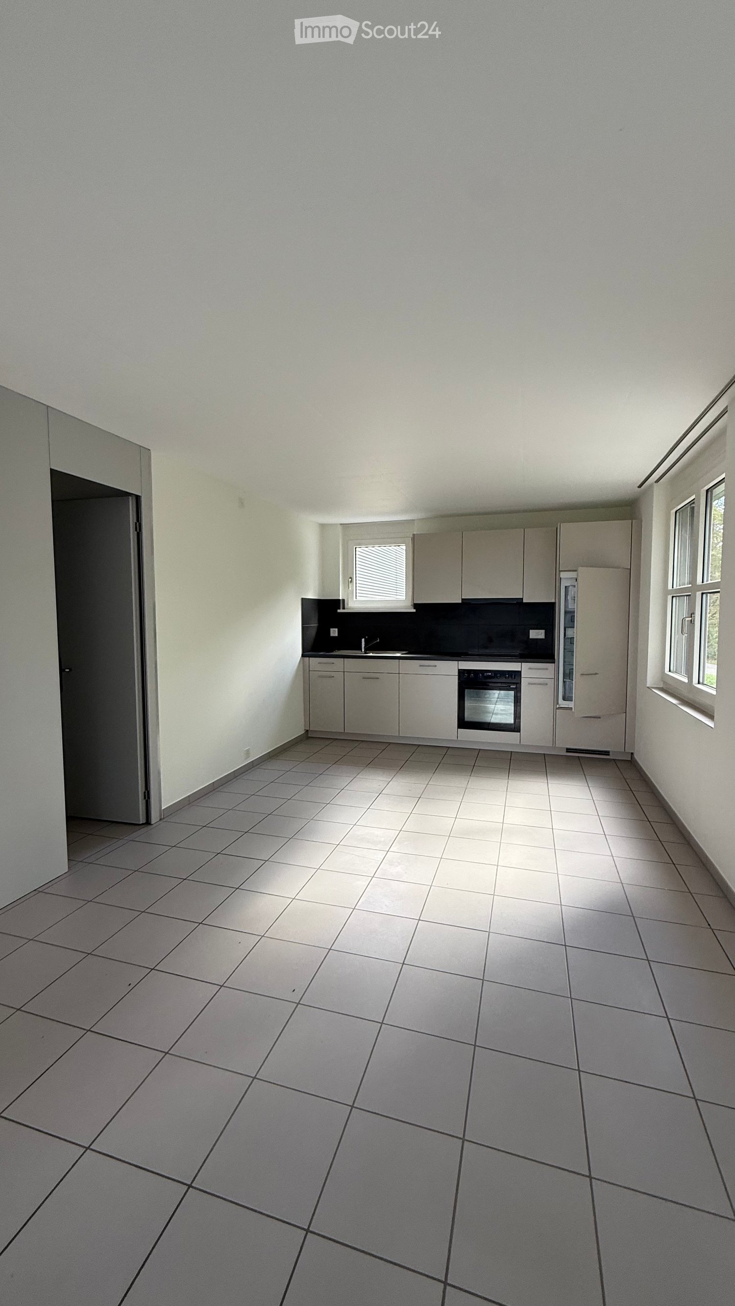 Empty kitchen with tiled floor, white cabinets, sink, oven, and refrigerator.