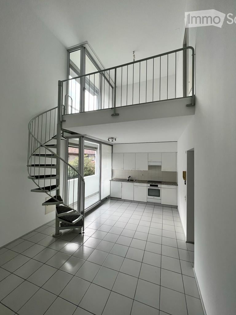 Open-plan space with a modern spiral staircase leading to an upper level, white tiled floor, white kitchen cabinets, and large windows allowing natural light.