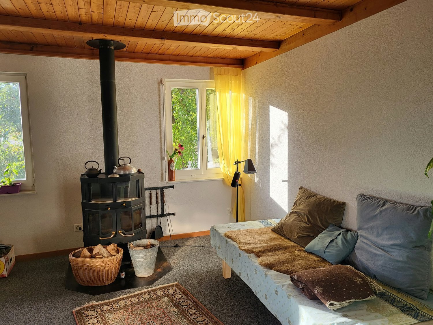 Cozy living space with a wood stove, sofa, teapots, wicker basket, and floor lamp.
